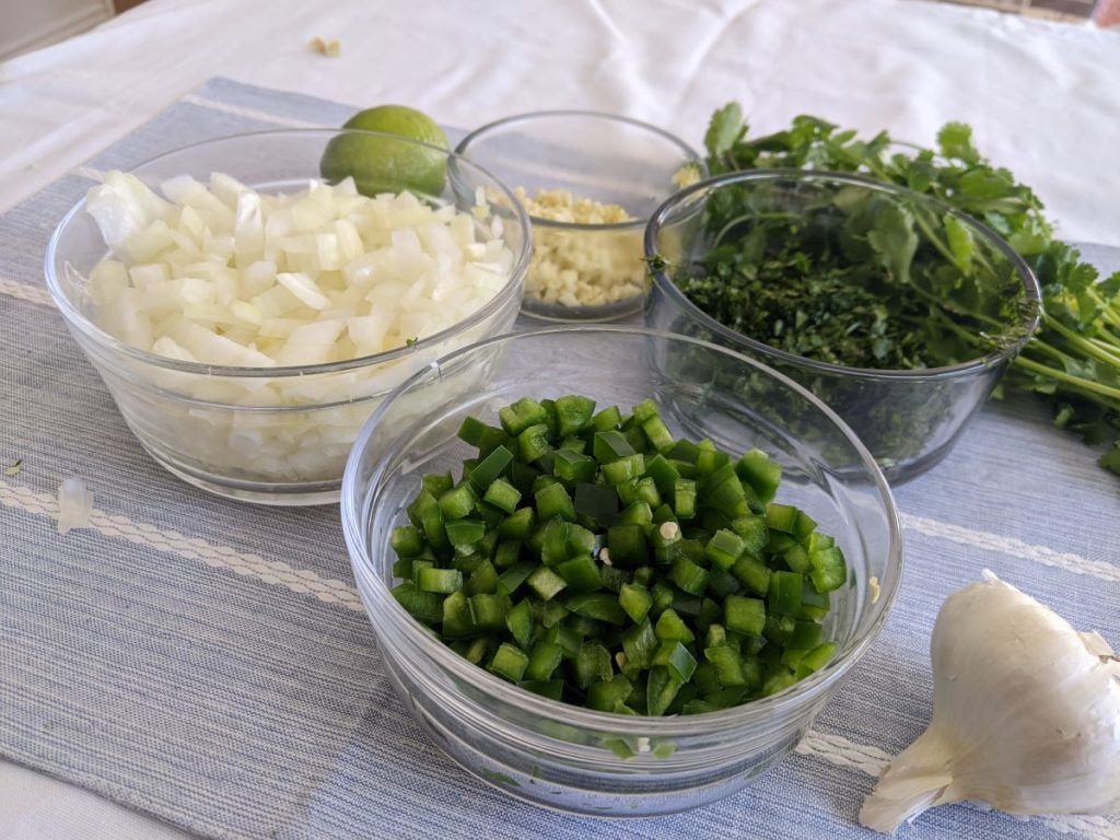 bowls of chopped jalapeno, onion, garlic, and cilantro on a table