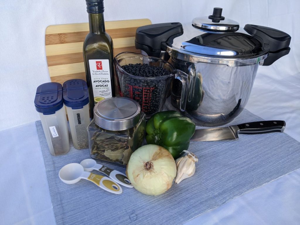 pressure cooker, black beans, spices, and veggies in front of a cutting board