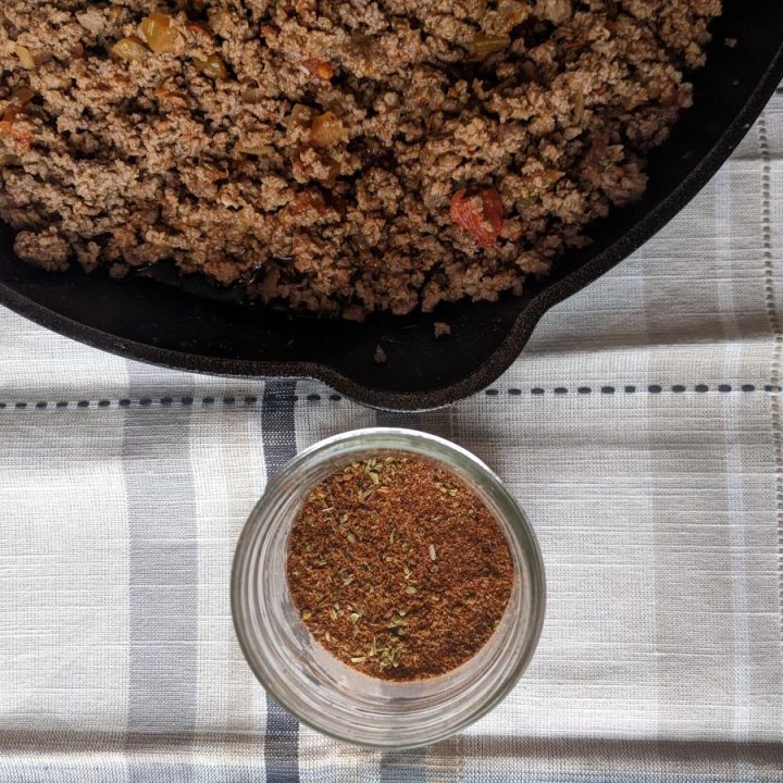taco meat in a cast iron pan with a jar of homemade taco seasoning next to in