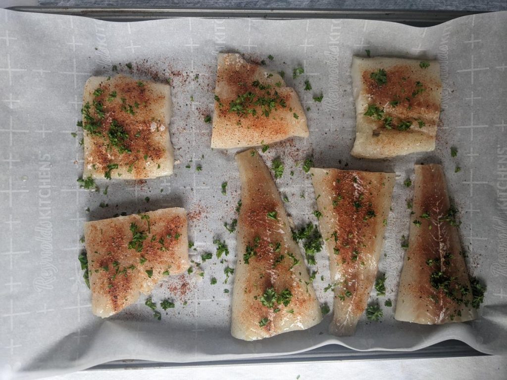 Cod seasoned and laying on a baking tray.