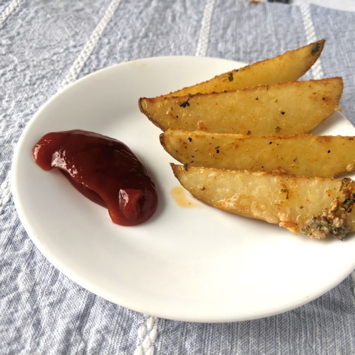 Four potato wedges on a plate with ketchup
