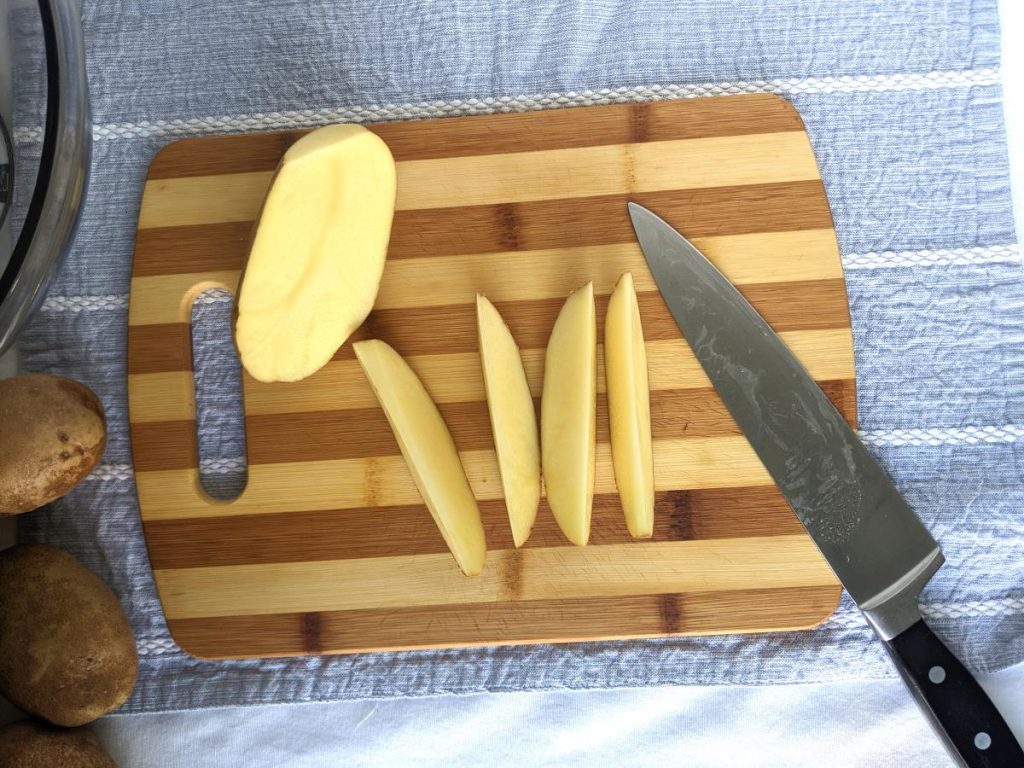 Potato wedges on a cutting board with a half of an uncut potato and a knife